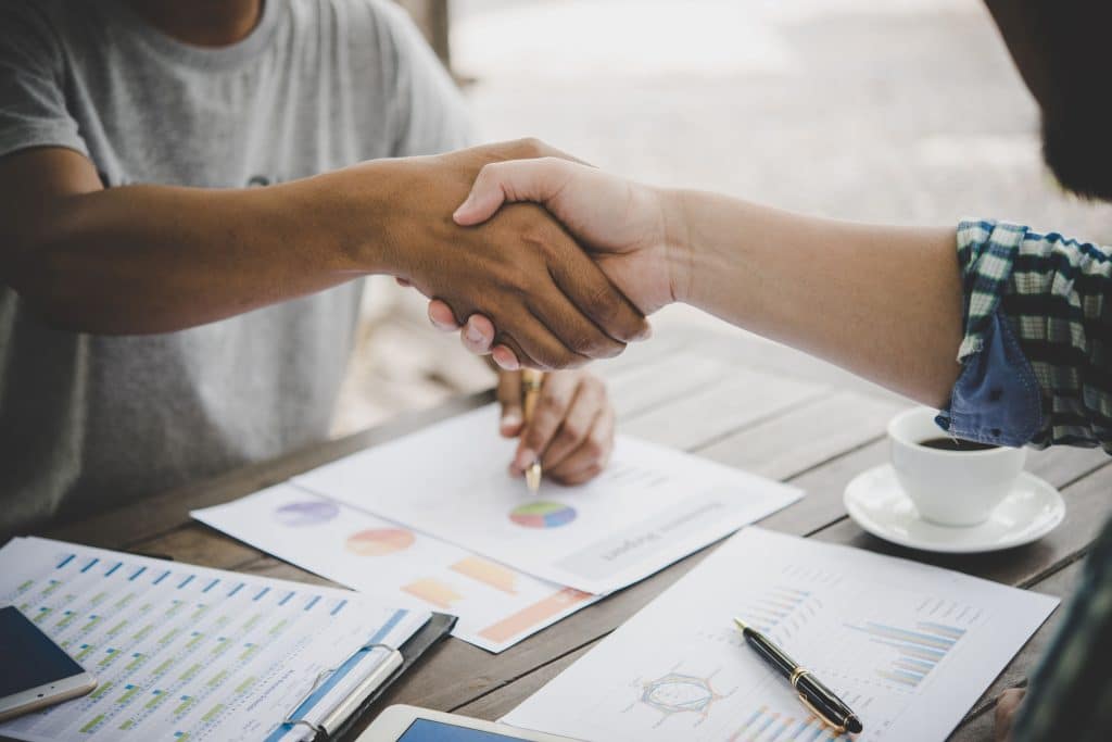 Business professionals shaking hands over financial charts and coffee, symbolizing successful brand partnerships and collaboration