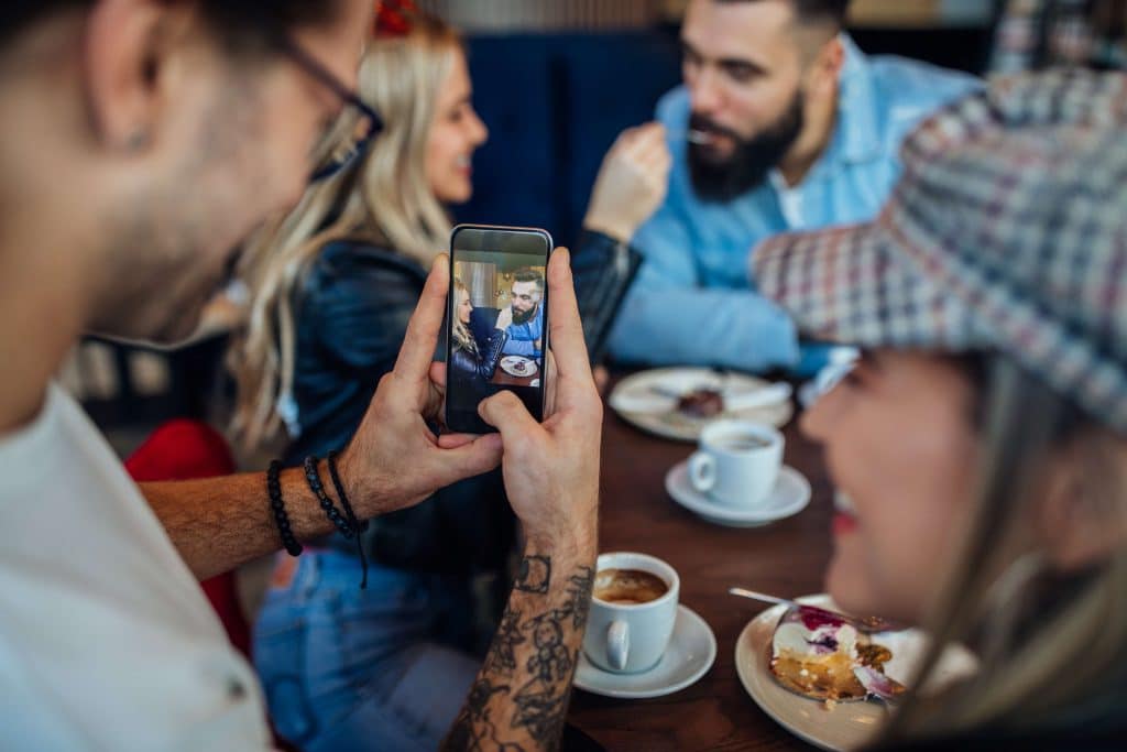 Person capturing user-generated content at a café, with coffee cups, dessert, smartphone, and creative atmosphere for social engagement