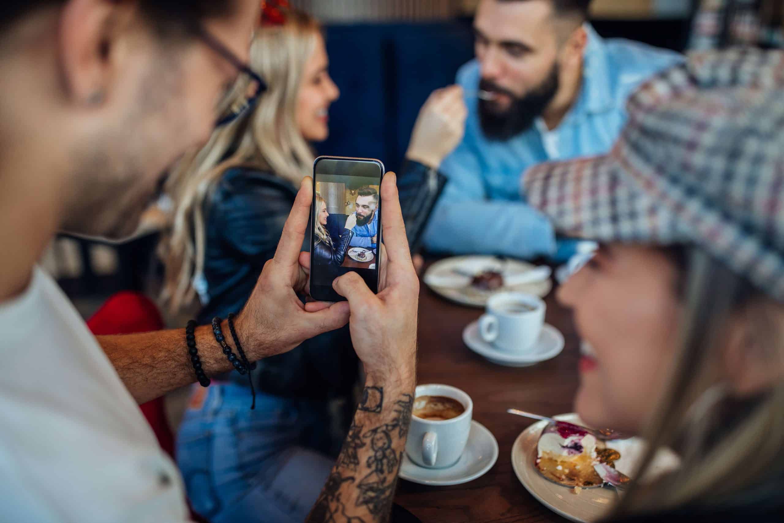 Person capturing user-generated content at a café, with coffee cups, dessert, smartphone, and creative atmosphere for social engagement